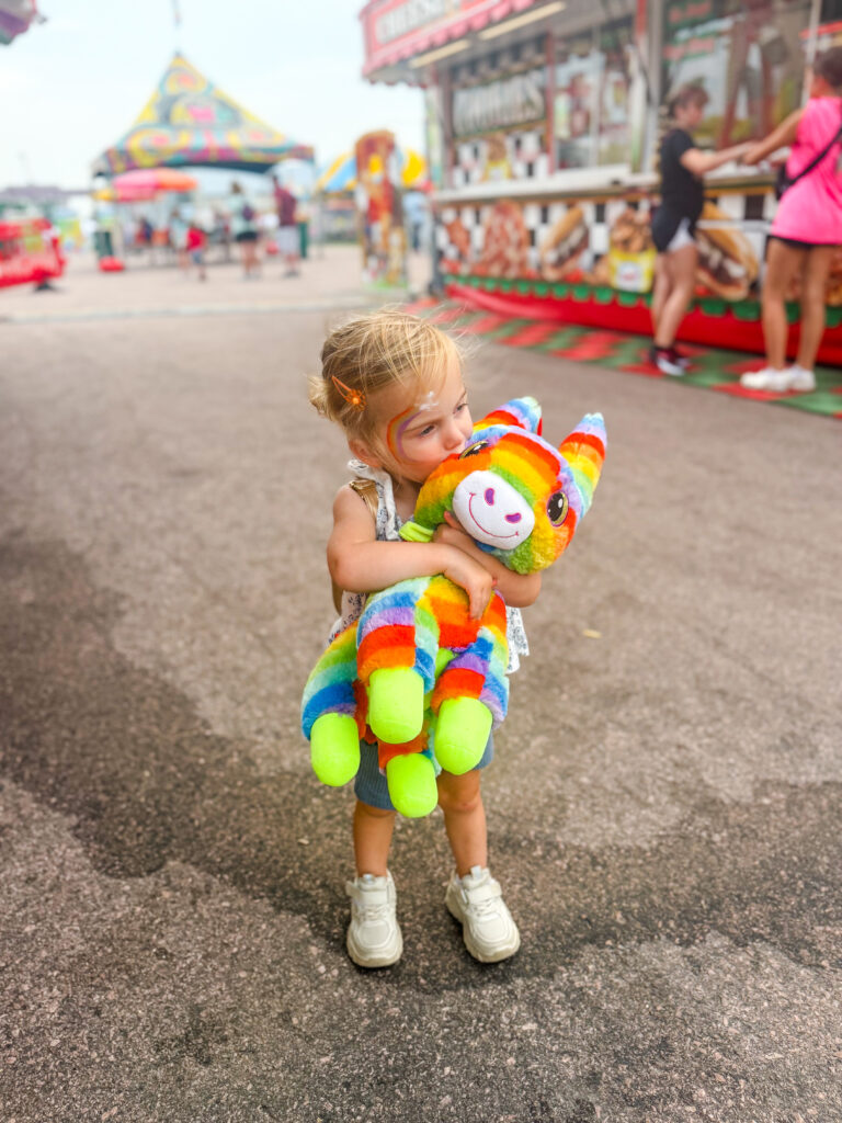 Photo of a little girl holding a stuffed animal at the fair
