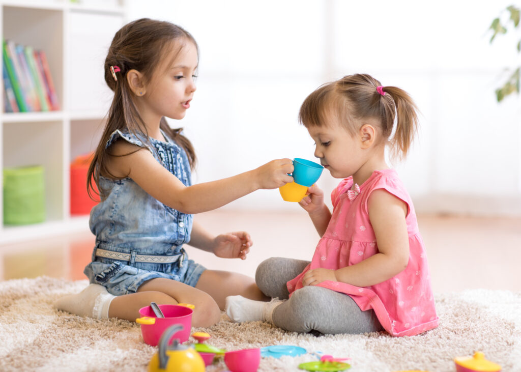 two toddler girls playing with a tea set