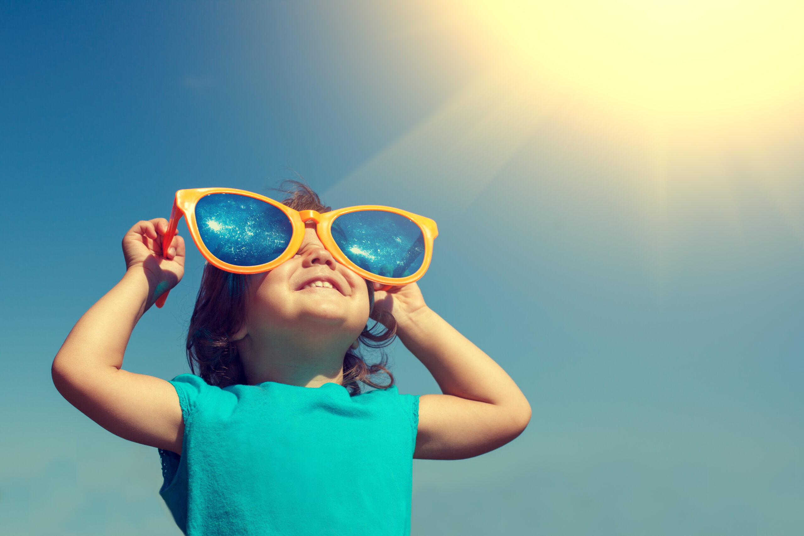 A girl looking up at the sun with big sunglasses to celebrate summer
