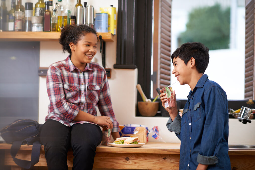 Shot of two young teenagers enjoying a snack together in the kitchen.