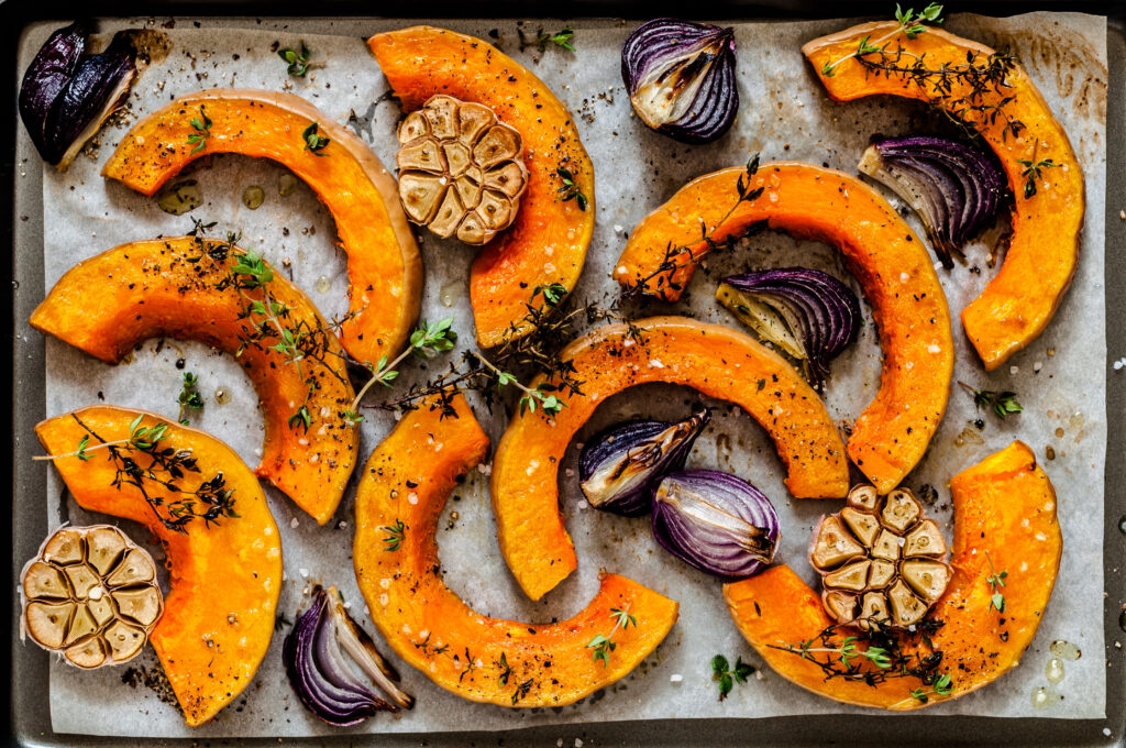 Roasted pumpkin on a tray with garlic and onions